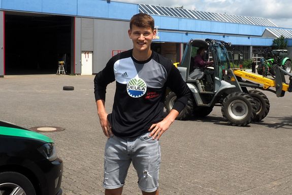 Praktikant Christoph Grimm vor den Hallen der DEULA, im Hintergrund Bagger und Traktor 